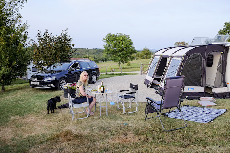 a lady outside her caravan with her dog and a bottle of wine