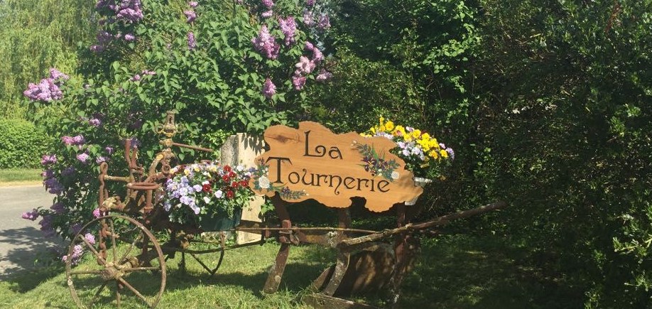 The sign welcomes you to the entrance of the site: "La Tournerie". It is hung from an old plough and is decorated with flowers