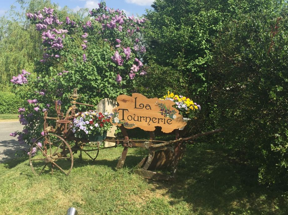 The sign welcomes you to the entrance of the site: "La Tournerie". It is hung from an old plough and is decorated with flowers